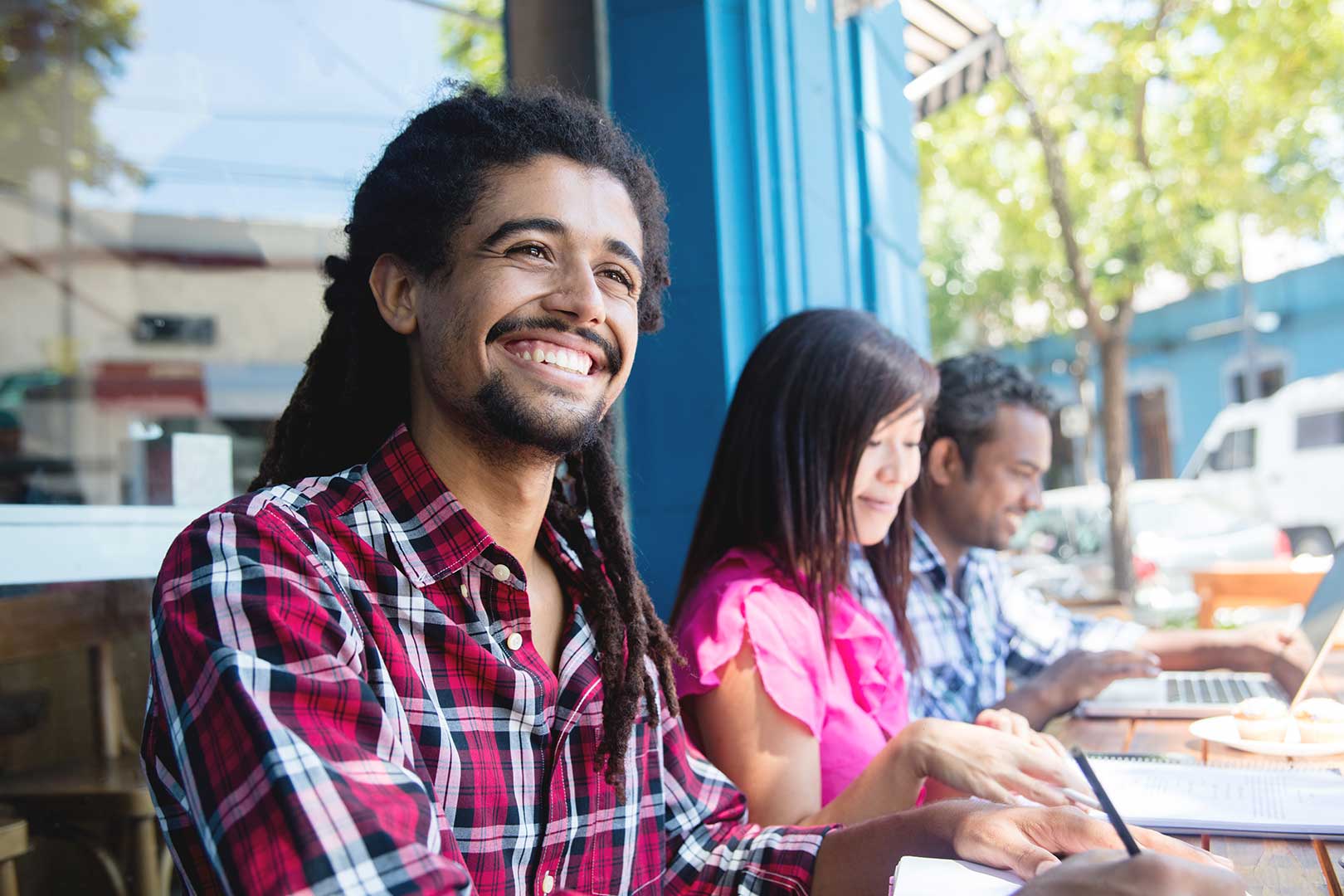 Three people sitting outdoors on a computer and taking notes