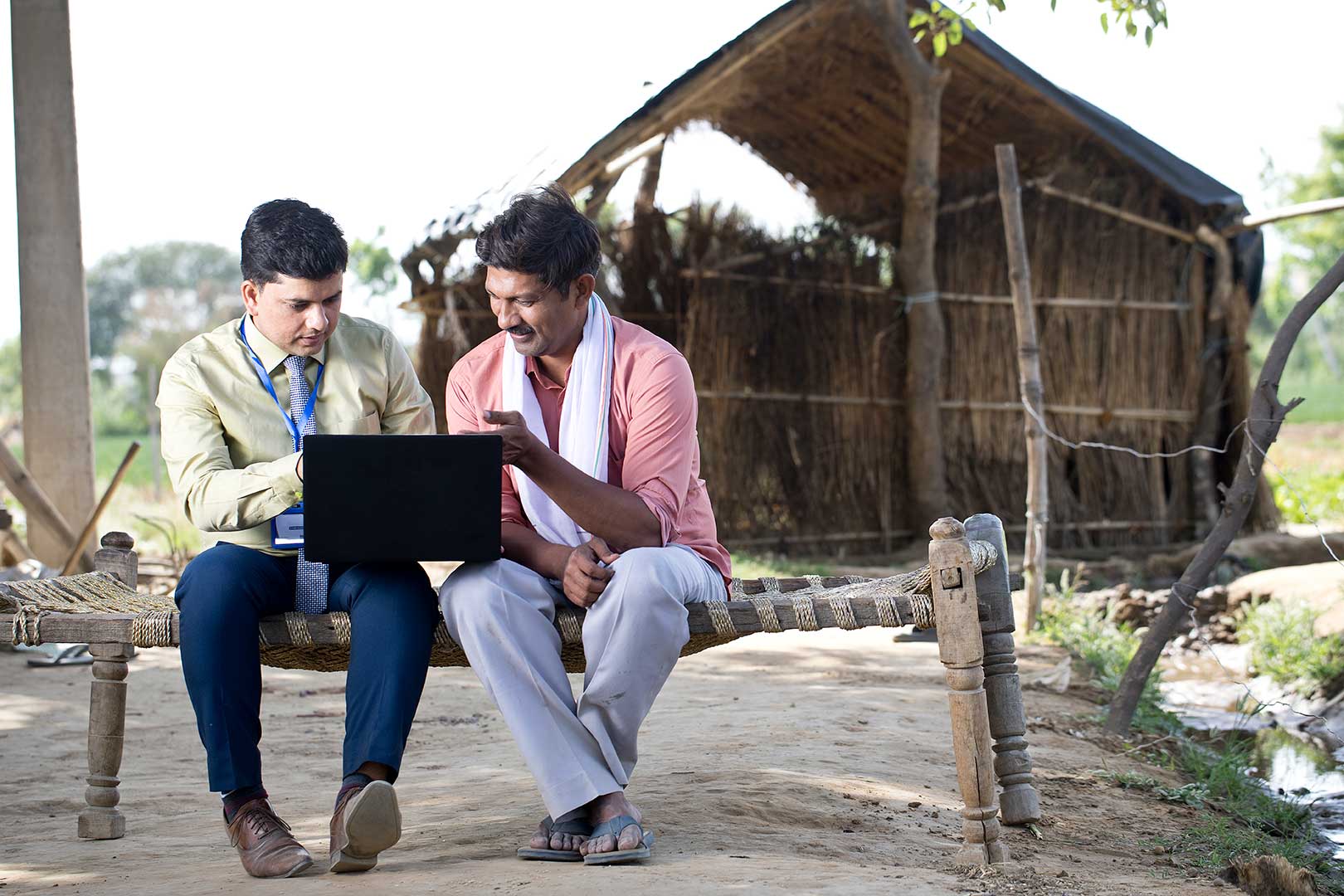 Two people sitting on a bench outdoors looking at a computer